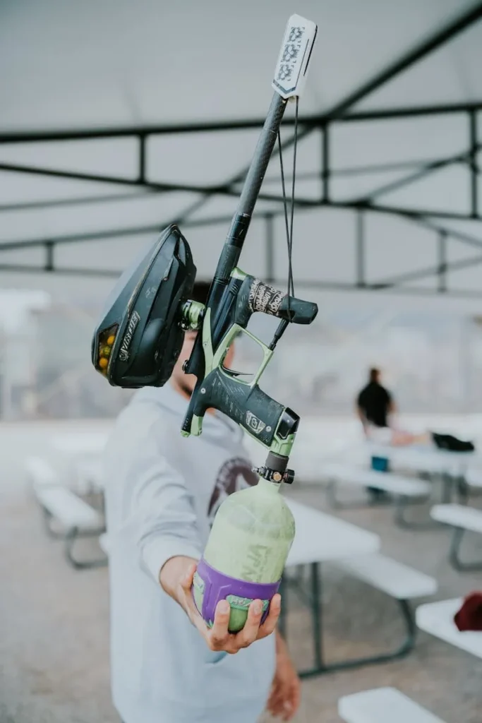 A person casually holding a paintball gun outdoors, focused on equipment details.